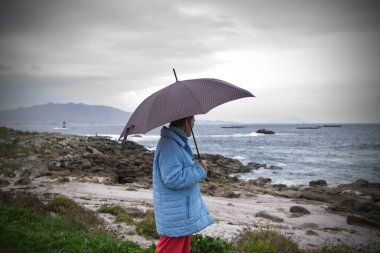 Sahilin önündeki ceketli ve şemsiyeli kadın.