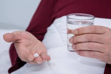 Bir bardak su ve hapla yatakta bir adam.