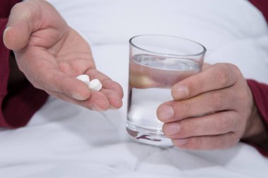 Bir bardak su ve hapla yatakta bir adam.