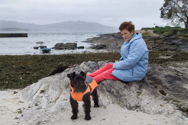 senior woman and her dog in coat looking at the sea