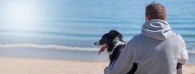 man sitting in front of the sea on the beach with his dog friend