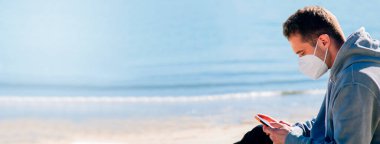 man with medical mask on the beach using the phone in the new normal