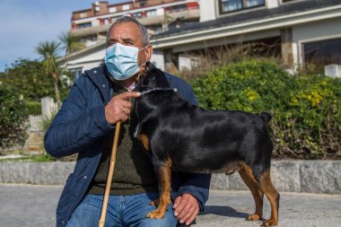 Tıbbi maskeli yaşlı adam kendini sokaktaki koronavirüsten ve köpeğinden koruyor.