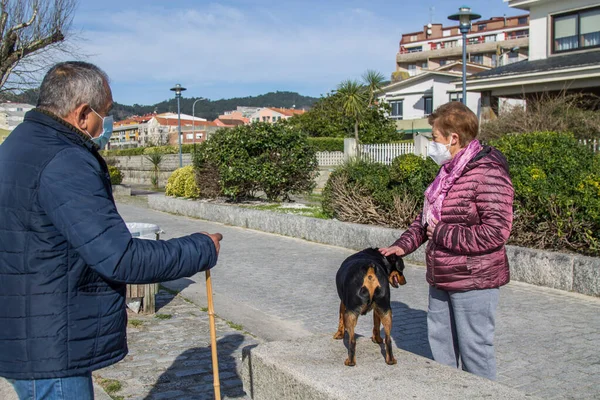 two senior people with medical mask and dog on the street keeping the safety distance and greeting each other