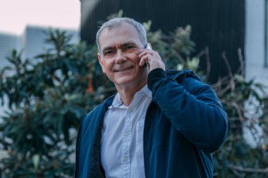 Yetişkin bir adam sokakta cep telefonuyla konuşuyor.