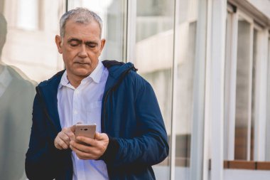 Yetişkin bir adam sokakta akıllı telefonunu kontrol ediyor.
