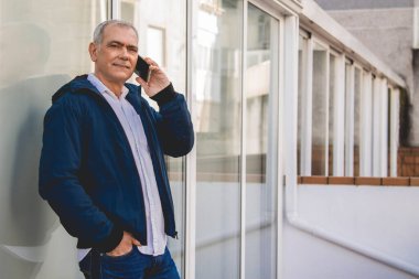 Ceketli yetişkin adam telefonuyla konuşuyor.