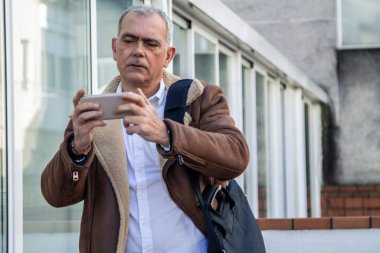 Dizüstü bilgisayar taşıyan ve şehirde cep telefonu kullanan bir adam.