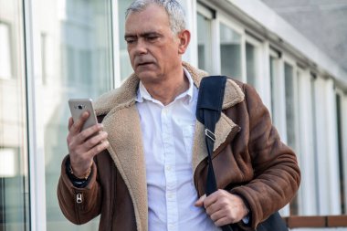 Dizüstü bilgisayar taşıyan ve şehirde cep telefonu kullanan bir adam.