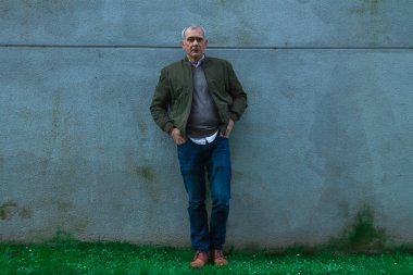 Sıradan giyinmiş yetişkin bir adam duvara yaslanıyor.