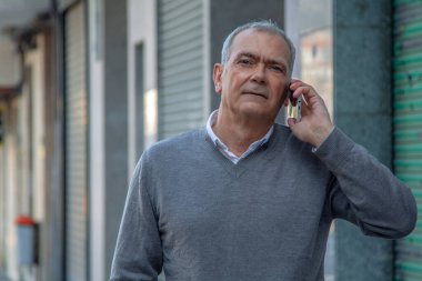 Yetişkin bir adam sokakta cep telefonuyla konuşuyor.