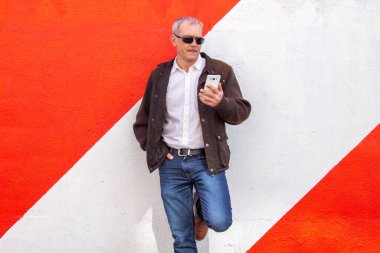 Yetişkin adam telefonu kullanarak duvara yaslanıyor.