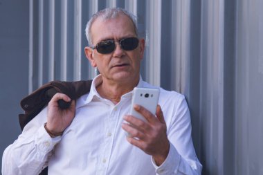 Omzunda ceketi olan yetişkin bir adam cep telefonunu kontrol ediyor.