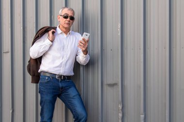 Yetişkin bir adam cep telefonu kullanarak duvara yaslanıyor.