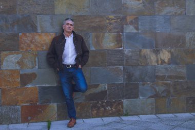 Duvarda kot pantolon ve ceket giyen yetişkin bir adam.