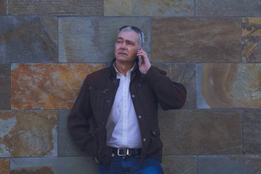 Duvarda cep telefonu kullanan yetişkin bir adam.