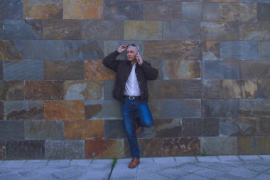 Duvarda cep telefonu kullanan yetişkin bir adam.