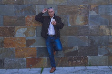 Sıradan bir yetişkin adam duvarda cep telefonu kullanıyor.