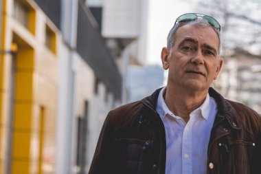 Şehirde yürürken ceketli olgun bir adamın portresi.