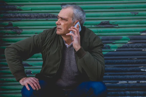 casual adult man squatting talking on his mobile phone with blind background