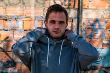 portrait of smiling man with sweatshirt on public wall with graffiti not subject to copyright