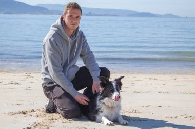 smiling man sitting on the beach with his dog