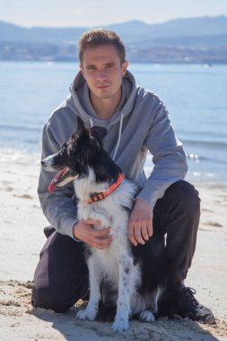 portrait of young man with his border collie dog on the beach