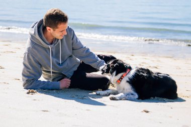 smiling man sitting on the beach with his dog