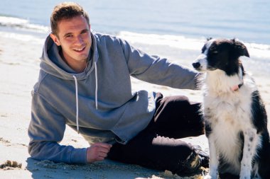 smiling man sitting on the beach with his dog