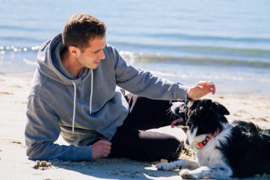 smiling man sitting on the beach with his dog