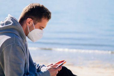 man with medical mask on the beach using the phone in the new normal