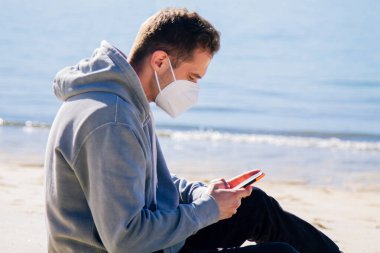man with medical mask on the beach using the phone in the new normal