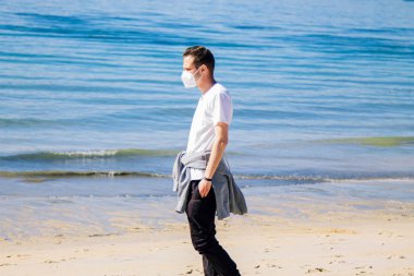 man with medical mask in protection of the coronavirus in the new normal walking on the beach