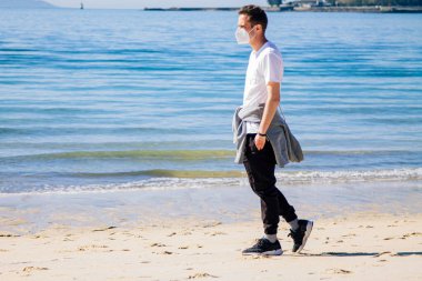 man with medical mask in protection of the coronavirus in the new normal walking on the beach