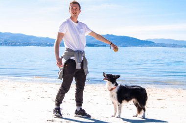 Genç adam sahilde köpeğiyle oynuyor.