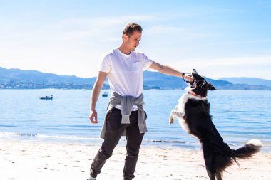 Genç adam sahilde köpeğiyle oynuyor.