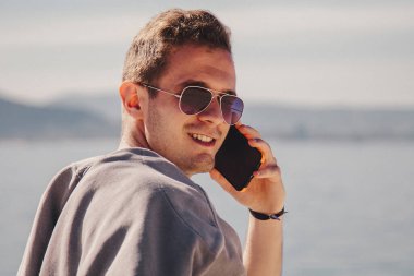man with sunglasses walking on the beach and talking on the phone