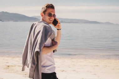 man with sunglasses walking on the beach and talking on the phone