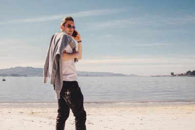 man with sunglasses walking on the beach and talking on the phone