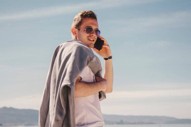 man with sunglasses walking on the beach and talking on the phone