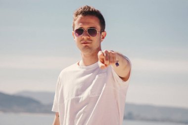 man with sunglasses walking on the beach and pointing a finger in a direction