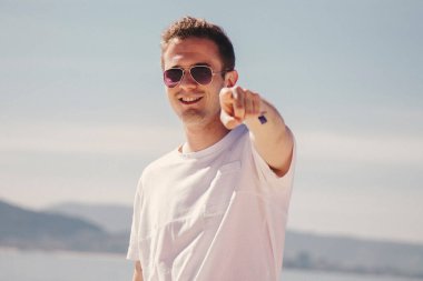 man with sunglasses walking on the beach and pointing a finger in a direction