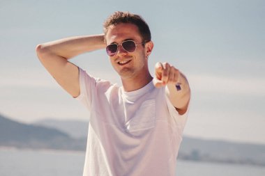 man with sunglasses walking on the beach and pointing a finger in a direction