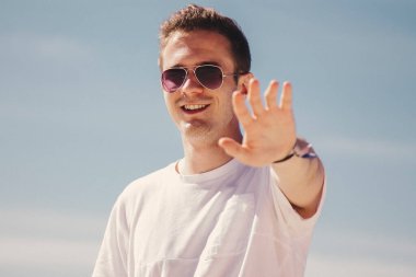 man in sunglasses walking on the beach and waving