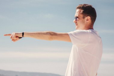 man with sunglasses walking on the beach and pointing a finger in a direction