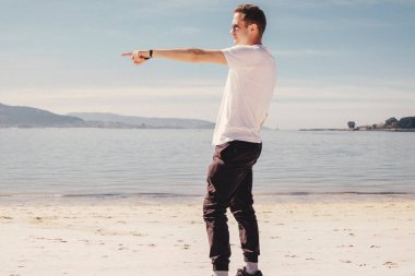 man with sunglasses walking on the beach and pointing a finger in a direction