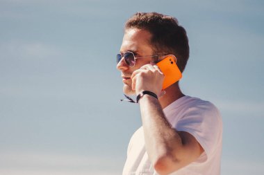 man with sunglasses walking on the beach and talking on the phone
