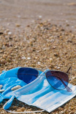 mask and surgical gloves with sunglasses on the beach sand