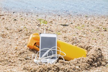 suntan lotion and mobile phone with headphones on the beach sand