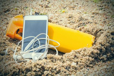 suntan lotion and mobile phone with headphones on the beach sand